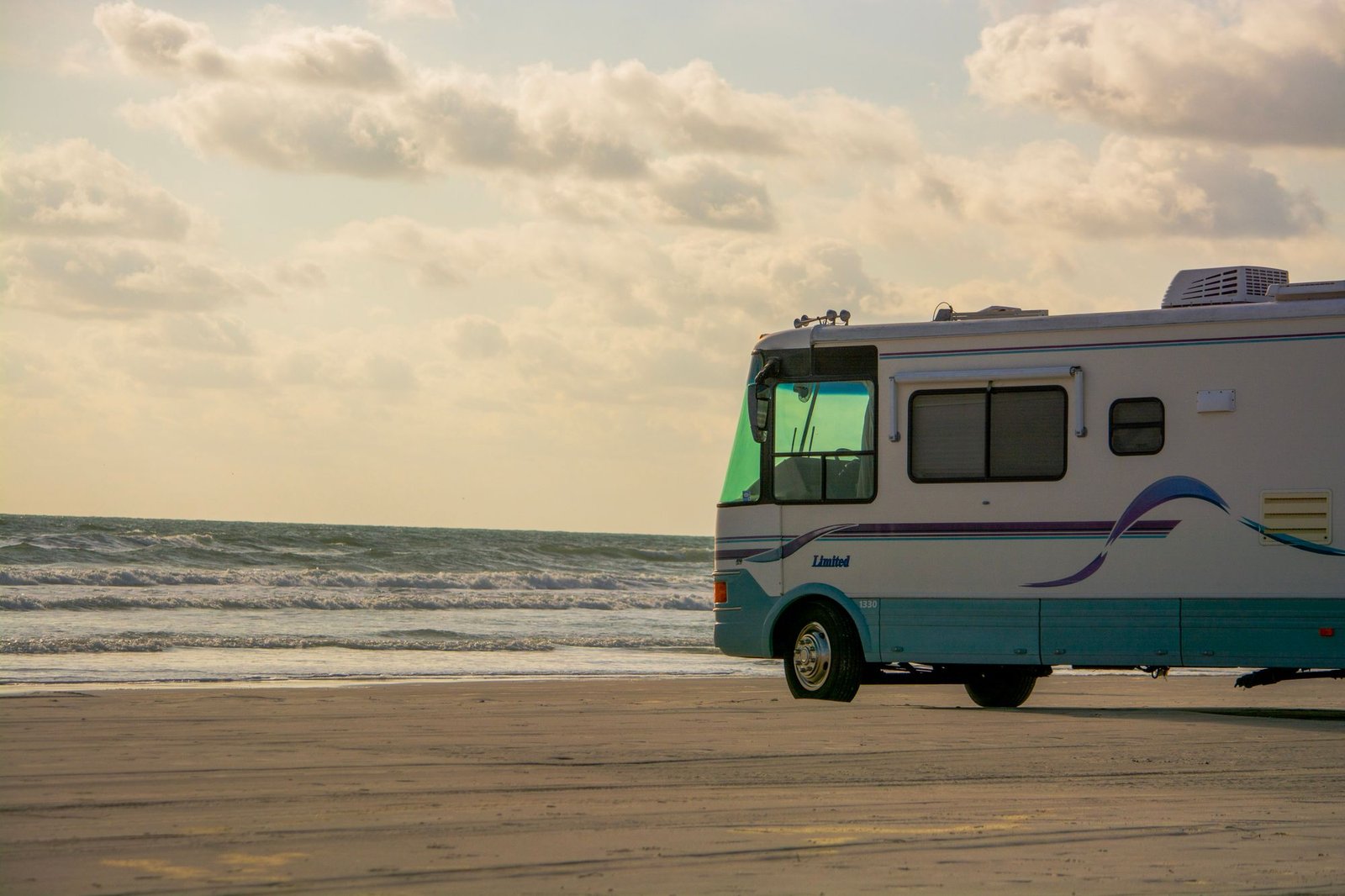 Class A motorhome parked on a beach under a golden sky